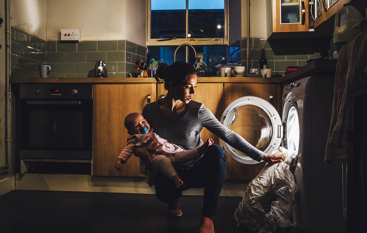 Jeune maman remplit la machine à laver d'un bras avec son bébé dans l'autre