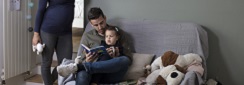 un papa lit une histoire à sa petite fille sous le regard attendri de la maman enceinte