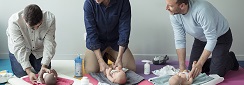 trois hommes dans un atelier de futurs papas apprennent à changer une couche sur des baigneurs