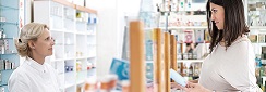 Femme enceinte au comptoir de la pharmacie regarde attentivement une boite qui lui est tendue