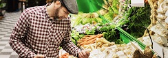 un homme au marché devant un étal de légumes racines