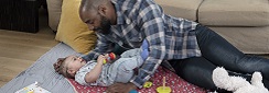 un papa joue avec un bébé par terre devant le canapé