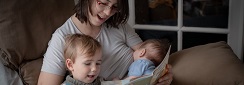 une maman lit un livre à son jeune fils en allaitant son bébé