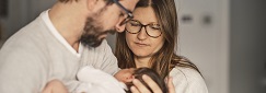 de jeunes parents regardent leur nourrisson tenu dans les bras du père