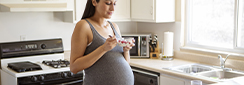 Une femme enceinte mange un fromage blanc aux fruits dans sa cuisine