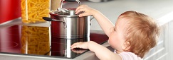 un très jeune enfant essaie d'enlever le couvercle d'une marmite sur une plaque de cuisson
