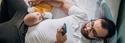 un papa regarde son smartphone alors que son bébé cherche à interagir avec lui