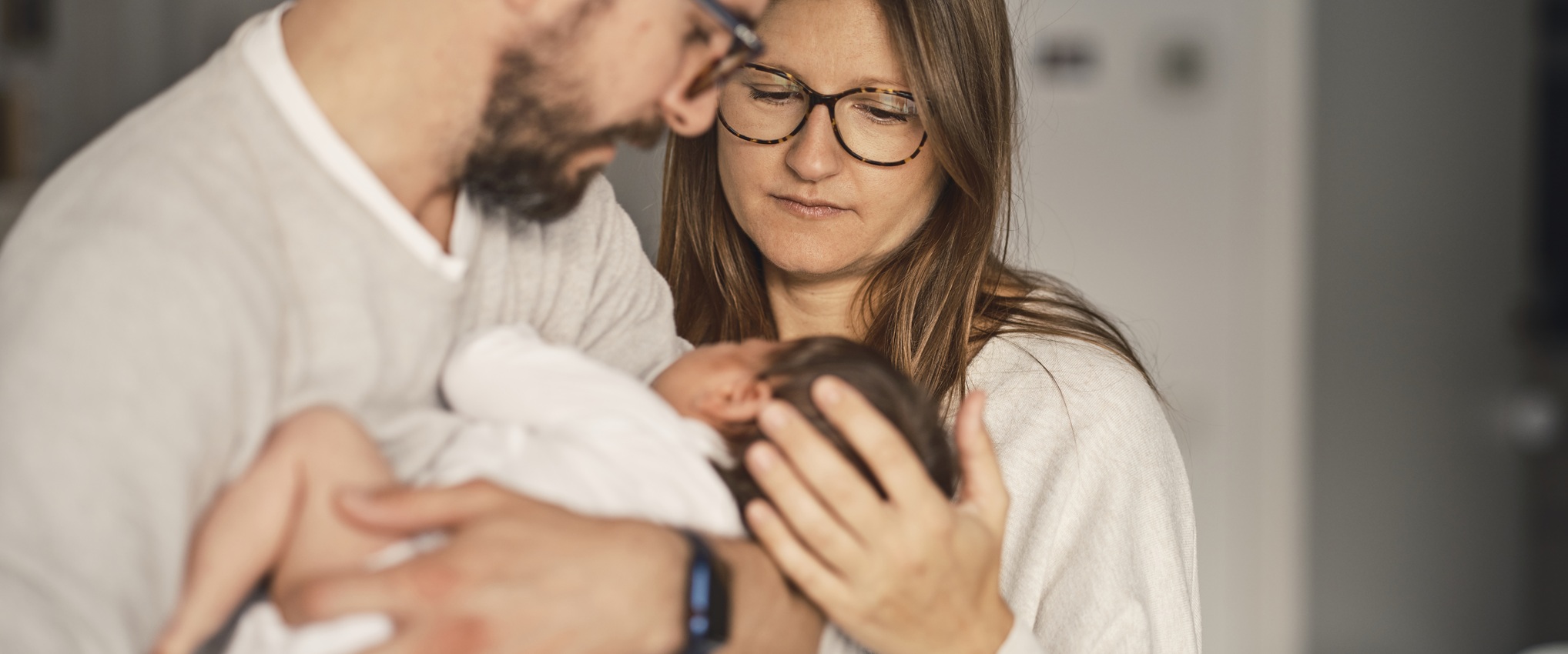 un couple regarde avec intensité un nourrisson dans les bras de l'homme