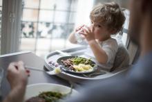 Un jeune enfant boit son verre d'eau devant son assiette, assis dans sa chaise bébé