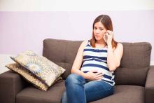 Une femme enceinte est au téléphone, assise sur son canapé