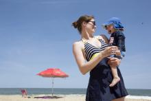 un bébé à la plage avec chapeau, vêtements couvrants et parasol