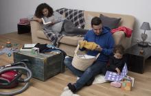 une femme enceinte lit sur le canapé pendant que son compagnon plie du linge à côté de leur petite fille